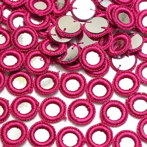 May include: A close-up of a pile of round, pink, crocheted embellishments with small, round mirrors in the centre.
