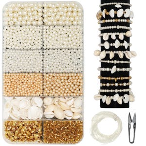 Puede incluir: Un kit para hacer joyas con varias cuentas, conchas y abalorios dorados. Incluye un organizador de plástico transparente lleno de cuentas blancas, crema y doradas, junto con conchas marinas. Varias pulseras de perlas y conchas se exhiben en un soporte negro, con hilo y tijeras.