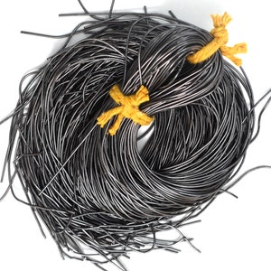 Op de afbeelding: Een grote bundel zwart lederen koord, gebonden met geel touw. Het koord is in een cirkelvormige vorm gerangschikt.