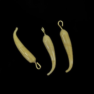 May include: Three light beige, curved pendants with gold-colored loops for hanging. The pendants have a smooth, glossy finish and are set against a black background. The shape resembles a chili pepper or a curved horn.