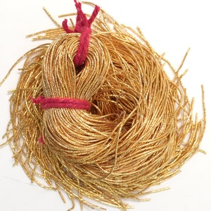 May include: A large spool of gold metallic cord, tied with a red string. The cord is made of thin, shiny, metallic threads.