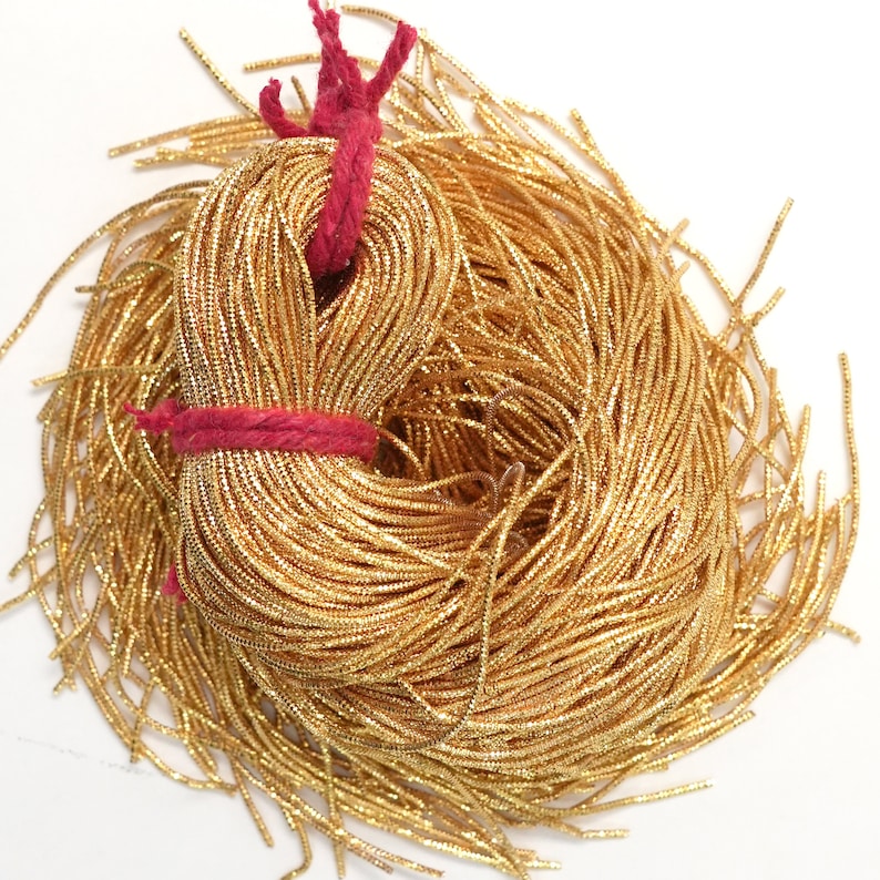 May include: A large spool of gold metallic cord, tied with a red string. The cord is made of thin, shiny, metallic threads.