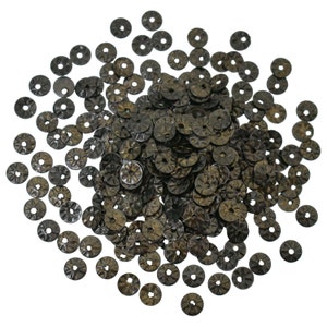 May include: A large pile of round, black metal sequins with a raised, textured design. The sequins are scattered on a white background.