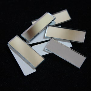 May include: A pile of small, rectangular mirror tiles. The tiles are silver and have a reflective surface.