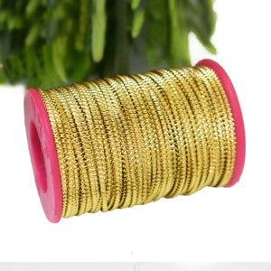 May include: A spool of gold metallic cord with a pink plastic bobbin. The cord has a textured, slightly raised pattern.