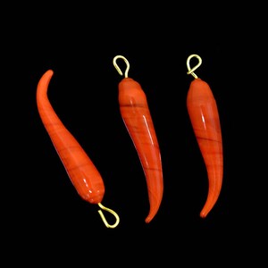 May include: Three red chili pepper shaped pendants with gold loops. The pendants are made of a smooth, shiny material.