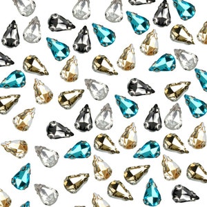 Puede incluir: Surtido de piedras de imitación en forma de lágrima en varios colores, incluyendo transparente, negro, dorado y azul. Las piedras de imitación están esparcidas sobre un fondo blanco.