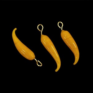 May include: Three yellow glass chili pepper charms with gold-colored metal loops.