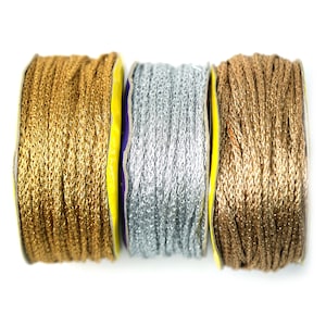 May include: Three spools of metallic thread, one gold, one silver, and one bronze. The spools are wound with the thread and have yellow and purple labels.
