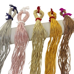 Puede incluir: Seis carretes de hilo de colores, cada uno de un color diferente: plateado, rosa, dorado, amarillo, marrón y morado. Los carretes están dispuestos en fila, con el carrete plateado a la izquierda y el carrete morado a la derecha.