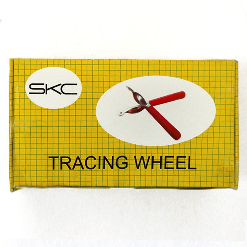 May include: A yellow box with a grid pattern and the text "SKC TRACING WHEEL". Inside the box is a red tracing wheel.