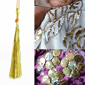 May include: A close-up of gold tassel trim with a gold cord. The tassel is made of thin, shiny strands of gold thread. The cord is tied in a knot at the top of the tassel. The tassel is on a white background.