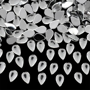 May include: A large quantity of clear teardrop-shaped rhinestones. The rhinestones are scattered on a black background.