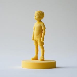 Op de afbeelding: Een gele beeldje van een jong kind, staand op een gele cirkelvormige basis. Het kind draagt een shirt met korte mouwen en een korte broek. Het beeldje is effen van kleur en heeft een gladde textuur. De achtergrond is effen wit.