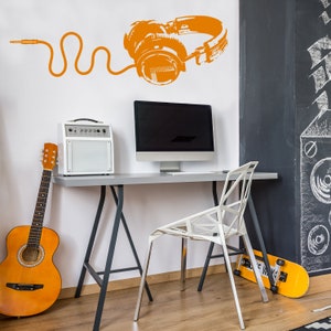 May include: A white desk with a black metal frame and a white chair. A computer monitor, a small amplifier, and a guitar are on the desk. A pair of headphones are on the wall behind the desk. The wall is painted white and has a black chalkboard on the right side.