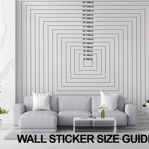 May include: A size guide for wall stickers, showing different sizes in inches and centimeters. The guide is displayed on a white wall with a gray couch in the foreground.