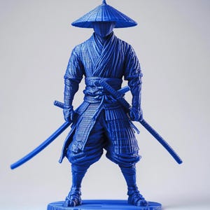 Op de afbeelding: Een blauw beeldje van een samoerai-krijger, compleet met een conische hoed en twee zwaarden. De figuur staat in een staande pose, met de zwaarden klaar. De samoerai draagt traditionele kleding en harnas.
