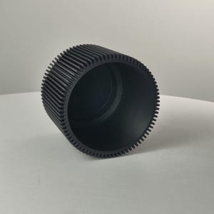 Pu&ograve; includere: Un componente cilindrico nero opaco caratterizzato da una serie di creste verticali lungo la superficie esterna. L'oggetto presenta un interno cavo con un'apertura circolare liscia e una base piatta, con una finitura scura uniforme su tutta la struttura.