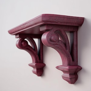Peut inclure: Une paire d'étagères murales décoratives en bois de couleur bordeaux. Chaque étagère est dotée d'un dessus rectangulaire soutenu par des supports ornés en forme de volute. Les supports présentent un veinage du bois.