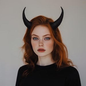 Puede incluir: Una mujer con el pelo largo y rojo que lleva una camisa negra y un par de cuernos de diablo negros.