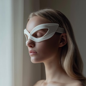 May include: A white superhero mask with a sleek, modern design. The mask features large eye openings and a strap that goes around the head. The mask is made of a smooth, matte material.