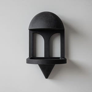 Puede incluir: Estantería de pared negra con diseño geométrico. Presenta una parte superior abovedada, dos aberturas arqueadas, una pequeña bandeja y una base puntiaguda. La veta de la madera es visible, añadiendo textura.
