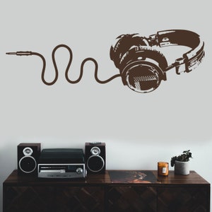 May include: A brown vinyl record player with two speakers on a wooden table. A brown silhouette of headphones with a cord is on the wall behind the record player.