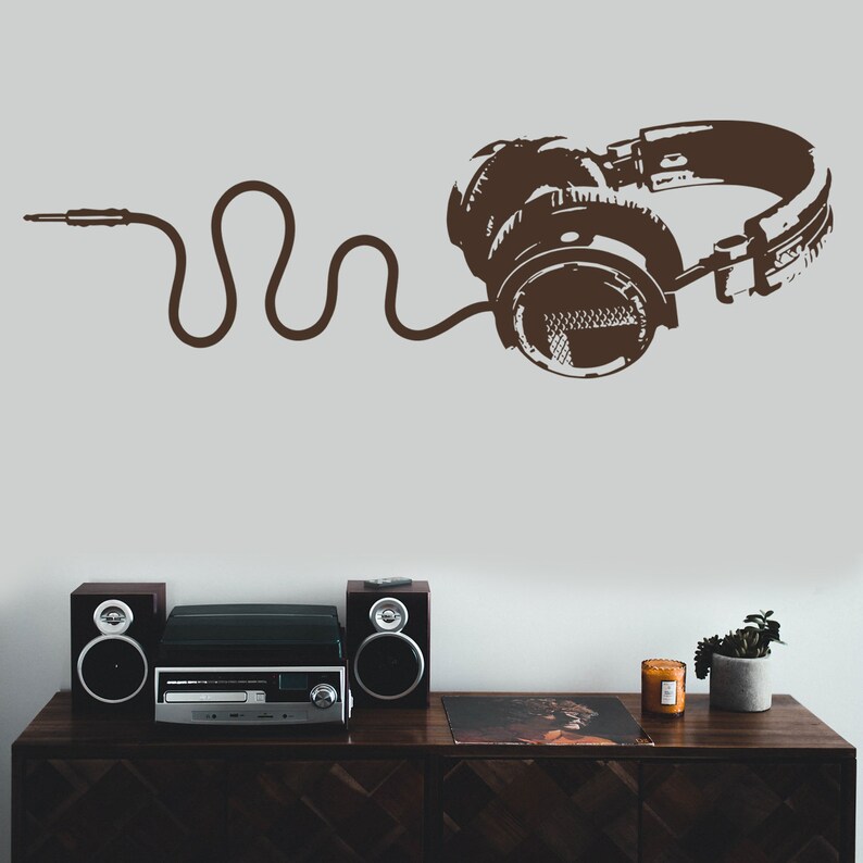 May include: A brown vinyl record player with two speakers on a wooden table. A brown silhouette of headphones with a cord is on the wall behind the record player.