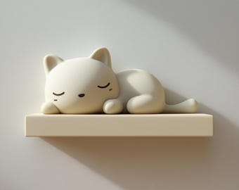 May include: A cream-coloured cat figurine in a sleeping pose, resting on a light beige shelf. The cat has closed eyes and a small black nose. The shelf is mounted on a white wall.