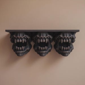 May include: A dark grey shelf featuring three monster mouth designs. Each mouth has rows of sharp teeth and a dark interior. The shelf is mounted on a neutral-coloured wall, creating a striking contrast.