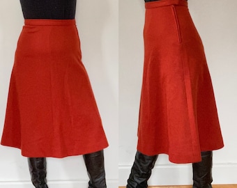 Op de afbeelding: Een roestkleurige midi-rok met een hoge taille en een lichte A-lijn. De rok is gemaakt van een dikke, gestructureerde stof en heeft een rits aan de achterkant.