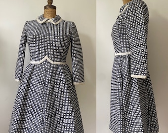 May include: A white and navy blue checkered dress with a white collar and white trim around the sleeves and waist.