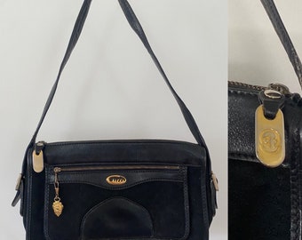 Könnte beinhalten: Eine schwarze Schultertasche aus Leder und Wildleder mit goldenen Beschlägen und einem Gucci-Logo. Die Tasche hat einen Reißverschluss und ein kleines Fach auf der Vorderseite.