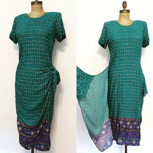 Könnte beinhalten: Ein blaugrünes Kleid mit geometrischem Muster und einem bunten Saum. Das Kleid hat einen Wickeldesign und einen kurzen Ärmel.