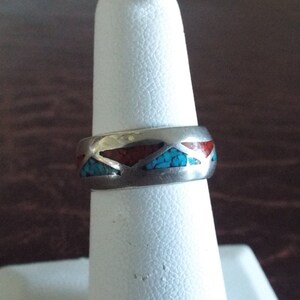 May include: A silver ring with turquoise and red stone inlay. The ring is on a white ring display stand.