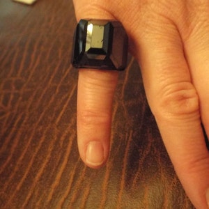 May include: A black ring with a large, faceted, rectangular stone.