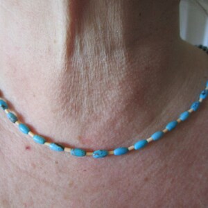 Puede incluir: Un collar de cuentas turquesa y blancas. El collar está hecho de pequeñas cuentas de forma ovalada. Las cuentas están enhebradas en un cordón delgado.