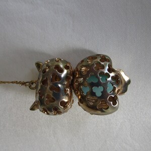 Pu&ograve; includere: Collana in tono oro con un ciondolo a forma di due cuori traforati, uno con un centro blu turchese.