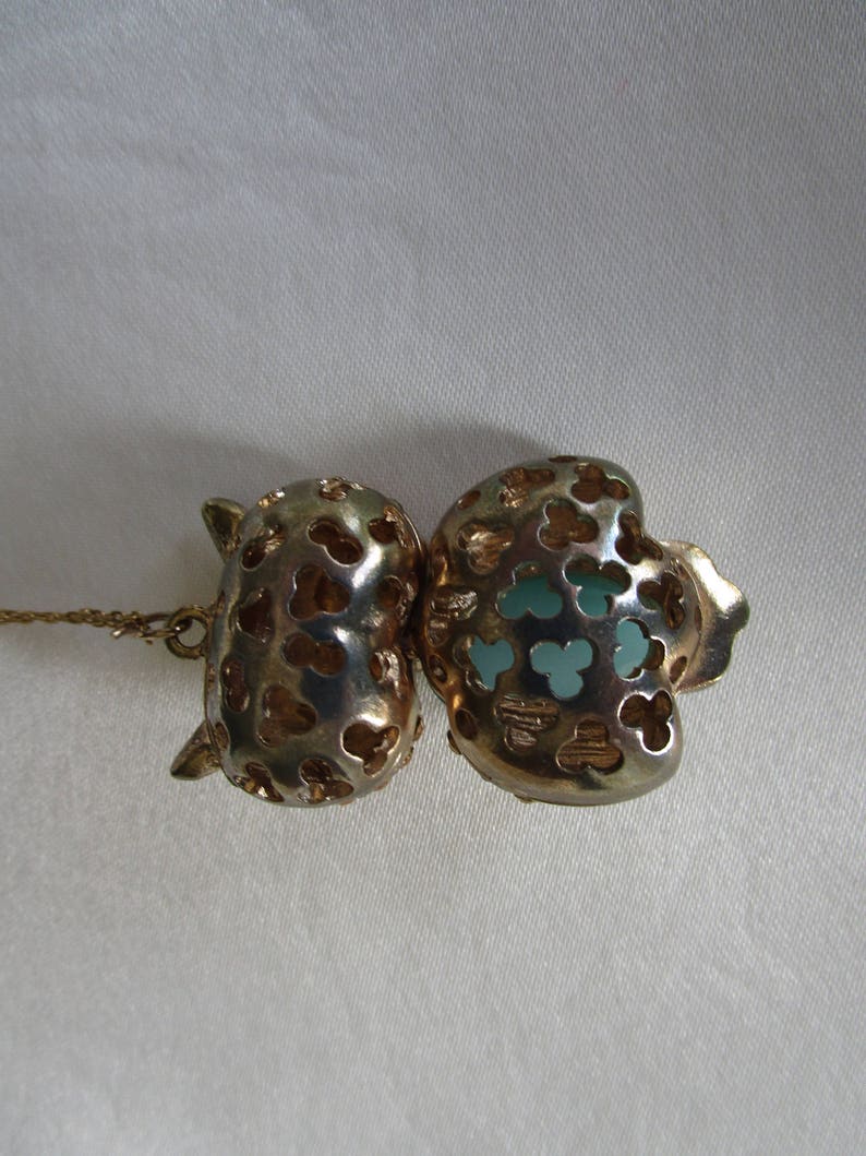 Pu&ograve; includere: Collana in tono oro con un ciondolo a forma di due cuori traforati, uno con un centro blu turchese.