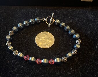 May include: A black hematite bead bracelet with silver accents and pink crystal accents. The bracelet is displayed on a black velvet surface with a US quarter for scale.