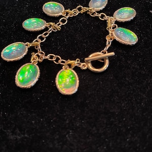 May include: A gold chain bracelet with multiple oval-shaped green and white iridescent charms. The bracelet has a toggle clasp.
