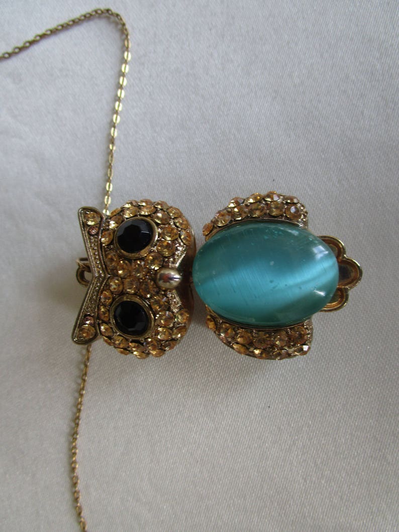 Pu&ograve; includere: Una collana con catena dorata con un ciondolo a forma di gufo. Il gufo &egrave; in metallo dorato e ha strass e pietre nere per gli occhi. Gli occhi del gufo sono blu e verdi.