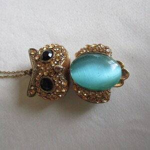 Pu&ograve; includere: Una collana con ciondolo a forma di gufo in oro, decorata con una pietra preziosa blu e strass trasparenti. Il gufo ha gli occhi neri ed &egrave; circondato da strass.