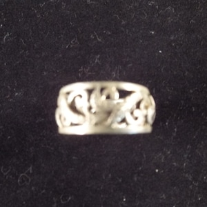 May include: A silver filigree ring with a delicate, intricate design. The ring is made of a thin band of metal with a pattern of swirls and curves.