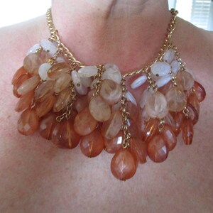 Peut inclure: Un collier en chaîne dorée avec un groupe de perles en cascade de pêche, orange et blanc.