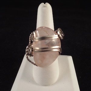 May include: A silver wire wrapped ring featuring a light pink oval shaped gemstone.