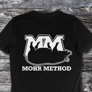 May include: Black t-shirt with a white graphic of a pig with the letters "MM" above it and the text "MOHR METHOD" below it.