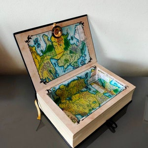 Puede incluir: Una caja negra con forma de libro con un mapa de Poniente en la portada y en el interior. La caja est&aacute; abierta y el mapa es visible en el interior. La caja tiene un cierre dorado y una cinta negra.