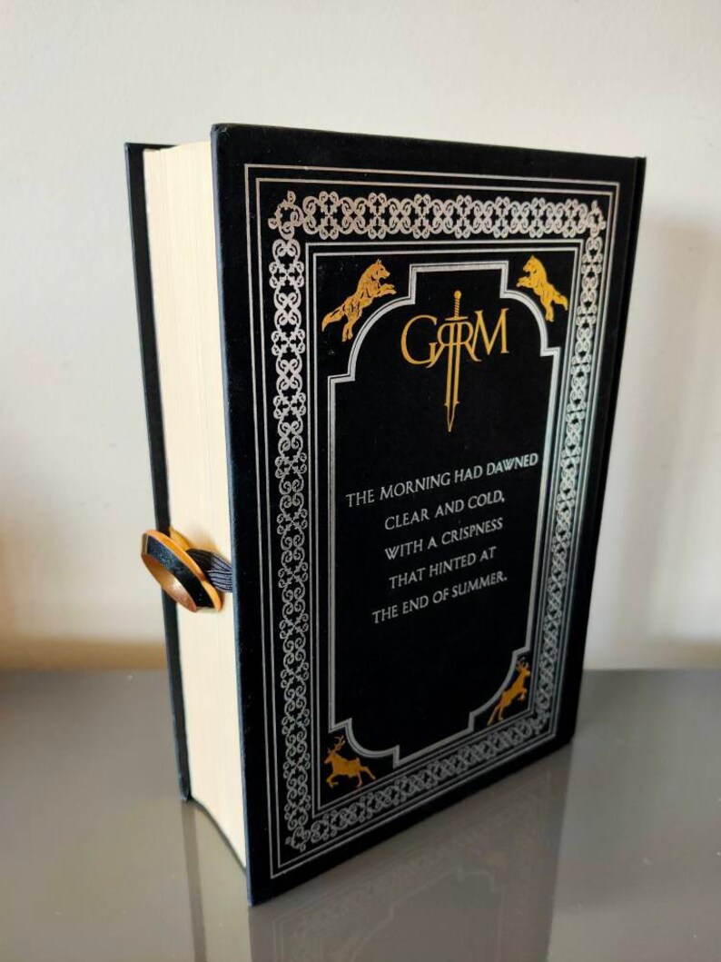 Puede incluir: Un libro de tapa dura negro con un dise&ntilde;o dorado y plateado. El t&iacute;tulo del libro es "GARM" y el texto de la portada dice "The morning had dawned clear and cold, with a crispness that hinted at the end of summer."