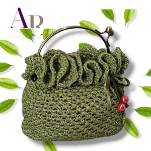 May include: A shimmering olive green crocheted handbag featuring a ruffled top edge, a metallic bronze circular handle, and a drawstring closure accented with two small, round, glossy red beads. The bag has a textured, open-weave pattern.